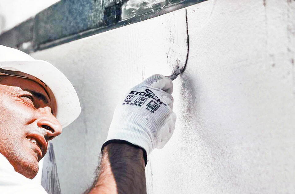 Handwerker bearbeitet mit einem Werkzeug den Verputz einer Mauer.