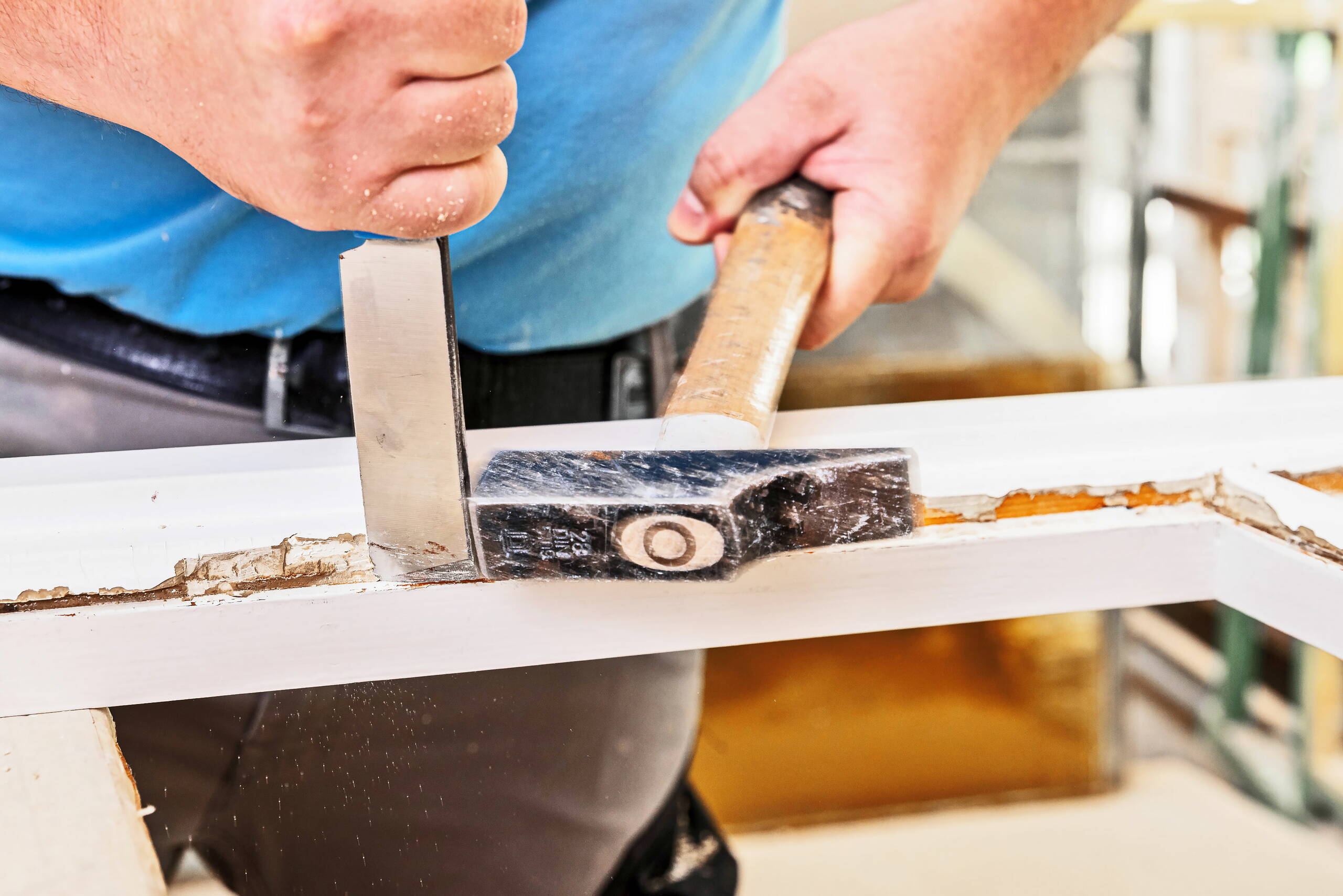 Fensterbauer bearbeitet mit einem Werkzeug einen Fensterrahmen aus Holz.